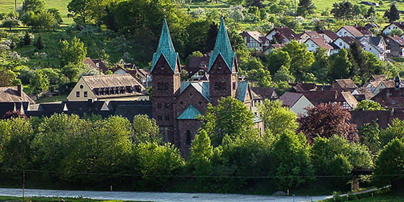 Die Klosterkirche zwischen Bäumen und den Häusern des Dorfes an den Hügeln des Spessart | © Bert Schwarz 2024